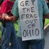 A man hangs an anti-fracking sign around a sign.